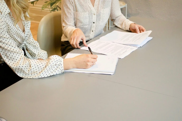 vrouw die op wit printerpapier tekent naast vrouw die op het punt staat de documenten aan te raken
